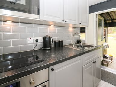 A kitchen countertop with a kettle two tins a sink and a stove next to an open door at 64 Penlan Holiday Park in Cenarth