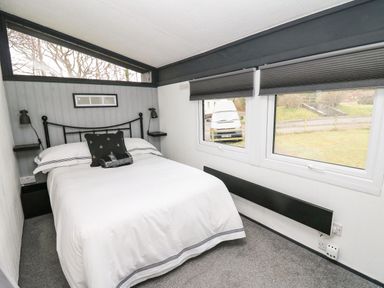 A bedroom with a bed and windows showing a parked van outside at 64 Penlan Holiday Park in Cenarth