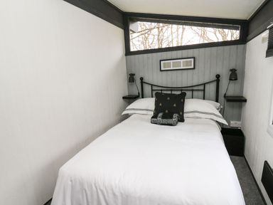 A small bedroom with a double bed white bedding and a black pillow under a window with trees outside at 64 Penlan Holiday Park in Cenarth