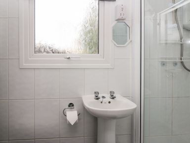 A bathroom with a white pedestal sink a frosted window a small octagonal mirror a toilet paper holder with a roll and a glass shower enclosure at 64 Penlan Holiday Park Cenarth