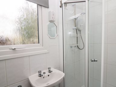 A bathroom with a shower enclosure and a small sink under a frosted window at 64 Penlan Holiday Park in Cenarth