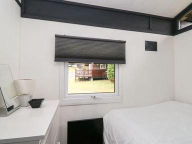 A bedroom with a bed white dresser mirror lamp and window with a blind at 64 Penlan Holiday Park in Cenarth