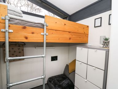 A small bedroom with a wooden loft bed ladder a gray chair with a pillow a white storage unit and two picture frames on the wall at 64 Penlan Holiday Park Cenarth
