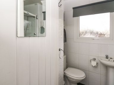 A bathroom with a toilet, sink, mirror, window with blind, and a shower enclosure at 64 Penlan Holiday Park in Cenarth