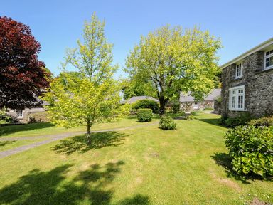 An outdoor garden area with trees shrubs grass stone pathways and stone buildings at Byre in Trethin near Camelford