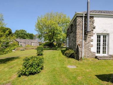 A garden with green grass shrubs and a large tree next to stone buildings at Byre in Trethin near Camelford