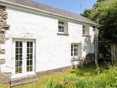 Exterior of a white stone house with three windows and a double glass door in a garden at Byre Trethin near Camelford