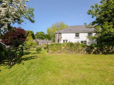 A grassy garden area with trees and a white stone house at Byre Trethin near Camelford
