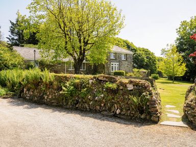 A stone house with trees and a stone wall at Byre in Trethin near Camelford