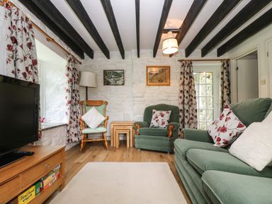 A living room with green upholstered seating floral curtains wooden beams and a television at Byre in Trethin near Camelford