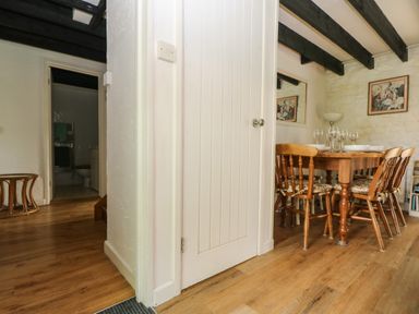 A dining area with wooden table and chairs beside a closed white door near a hallway with visible bathroom at Byre Trethin near Camelford