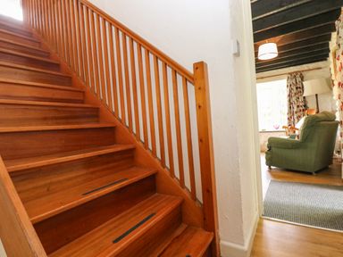 Wooden staircase next to a doorway leading to a room with a green armchair and patterned curtains at Byre Trethin near Camelford