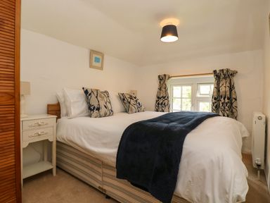 A bedroom with a double bed cushions a bedside table lamp and a window with curtains at Byre Trethin near Camelford