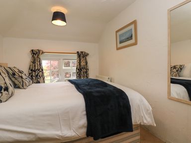 A bedroom with a bed pillows curtains window wall mirror and a framed picture at Byre Trethin near Camelford