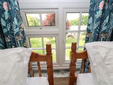 Two wooden beds with white bedding next to a window with blue curtains showing zebras at Byre Trethin near Camelford
