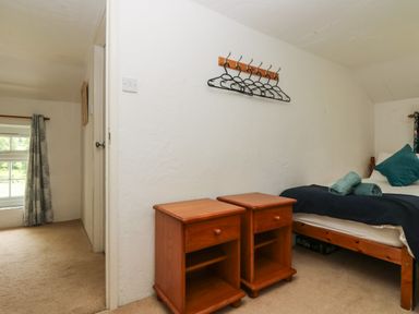 A bedroom with a single bed two wooden bedside tables and wall-mounted coat hooks at Byre Trethin near Camelford