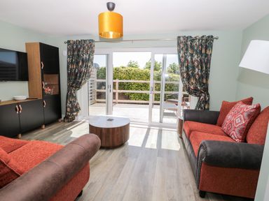 A living room with two red and brown sofas a round wooden coffee table floral curtains and sliding glass doors at Thrift Lodge in High Newton-by-the-Sea near Embleton