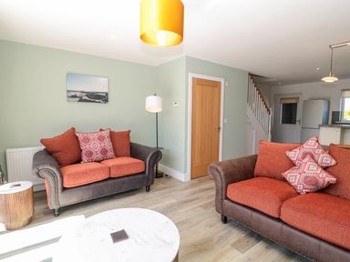 A living room with two sofas with orange cushions a round white coffee table and a door at Thrift Lodge in High Newton-by-the-Sea near Embleton
