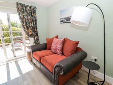 A living room with a sofa red cushions floor lamp side table and sliding glass door with curtains at Thrift Lodge in High Newton-by-the-Sea near Embleton