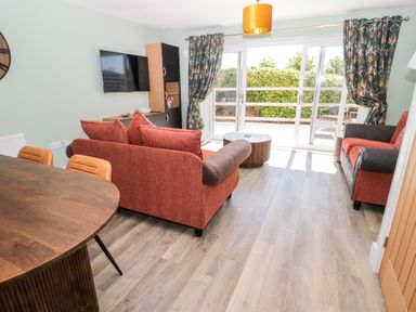 A living room with two red sofas a round wooden table a wall mounted TV and sliding glass doors at Thrift Lodge in High Newton-by-the-Sea near Embleton