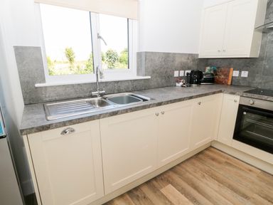 A kitchen with a double sink under a window and cream cabinets at Thrift Lodge in High Newton-by-the-Sea near Embleton