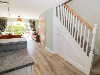An open living space with a staircase on the right and sofas near a sliding glass door at Thrift Lodge in High Newton-by-the-Sea near Embleton