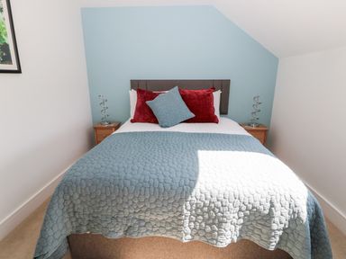 A bedroom with a bed with blue and red pillows and blue quilt at Thrift Lodge in High Newton-by-the-Sea near Embleton