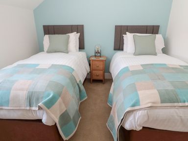 A bedroom with two single beds with patterned blankets and a wooden nightstand between them at Thrift Lodge in High Newton-by-the-Sea near Embleton