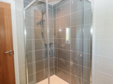 A shower enclosure with glass doors and grey tiled walls in a bathroom at Thrift Lodge in High Newton-by-the-Sea near Embleton