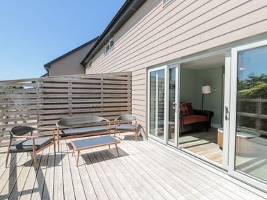 A wooden deck with outdoor furniture and sliding glass doors opening to a living room at Thrift Lodge in High Newton-by-the-Sea near Embleton