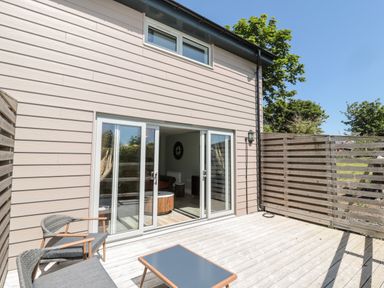 An outdoor patio with wooden floor and fence and sliding glass doors opening to a living room at Thrift Lodge in High Newton-by-the-Sea near Embleton