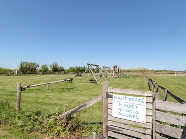 A children's playground with swings slide and seesaw behind a wooden gate with a no dogs allowed sign at Thrift Lodge in High Newton-by-the-Sea near Embleton