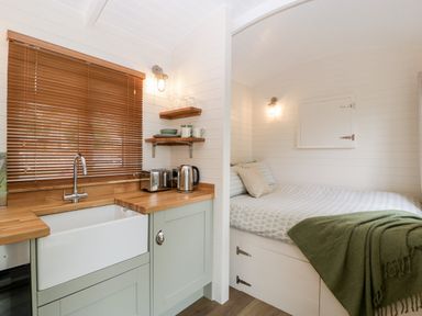 A small kitchen with wooden countertops next to a bed with a green blanket at Beech in Kemble