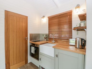 A kitchen with wooden door wooden countertop and wooden blinds on the window at Beech in Kemble