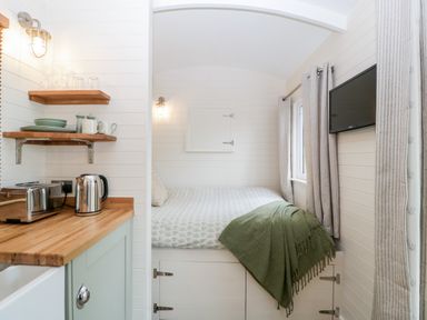 A small kitchen area with wooden countertop and appliances next to a bed with green blanket and a wall mounted TV at Beech in Kemble