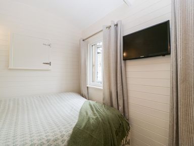 A bedroom with a bed covered with patterned sheets and a green blanket a window with curtains and a wall-mounted tv at Beech in Kemble