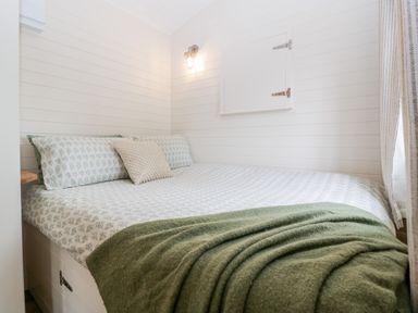 A bedroom with a bed covered in patterned bedding and green blanket with wall light and window at Beech in Kemble