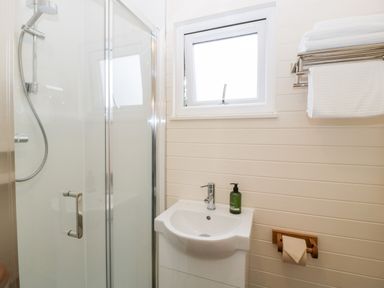 A bathroom with a glass shower cubicle a white sink with a soap dispenser a small window towel rack with towels and a toilet paper holder at Beech in Kemble