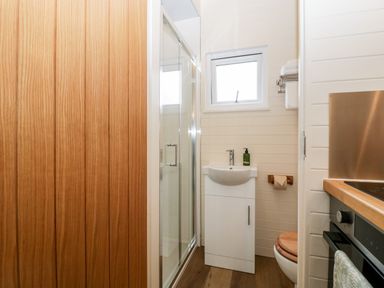 A small bathroom with a wooden door a shower with glass doors a white sink a window and a toilet with a wooden seat at Beech Kemble