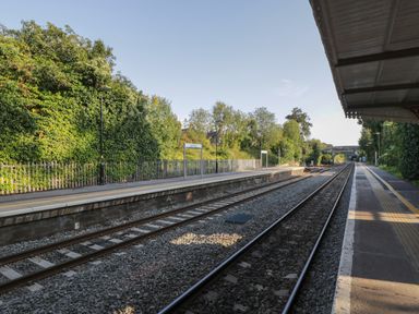 A railway platform with train tracks and trees in the background at Beech in Kemble