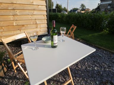 A white outdoor table with two wooden folding chairs a bottle of wine two wine glasses and a bowl on a stone-covered patio at Beech in Kemble