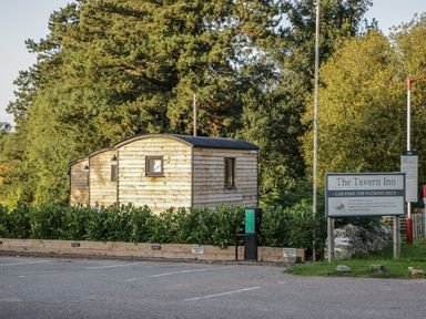 A parking lot with wooden cabins and a sign for The Tavern Inn at Beech in Kemble