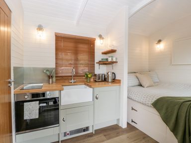A small kitchen area with wooden countertop and sink next to a bed with patterned bedding and a green blanket at Hazel Kemble