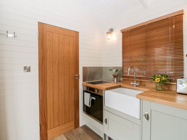 A kitchen with a wooden door a sink oven and utensils on the counter at Hazel in Kemble