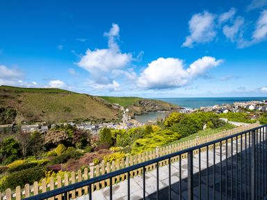 A view from a balcony overlooking a hillside with shrubs and houses by a bay and the ocean at Harbour Lights Port Isaac
