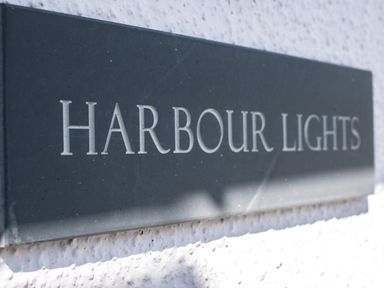 A black sign with white letters reading Harbour Lights mounted on a white textured wall at Harbour Lights Port Isaac
