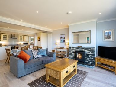 A living room with a blue sofa and wooden coffee table near a stone fireplace and TV at Harbour Lights Port Isaac