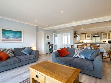A living room with two gray sofas and a wooden coffee table adjacent to a dining area and kitchen at Harbour Lights Port Isaac