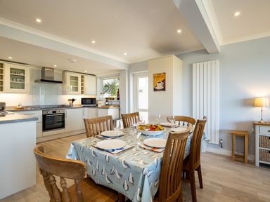 A kitchen and dining area with a table set for six and wooden chairs at Harbour Lights Port Isaac