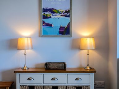 A console table with three drawers and wicker baskets with two lamps and a framed Port Isaac Cornwall poster on the wall at Harbour Lights Port Isaac